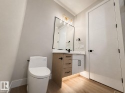 Modern bathroom featuring a two-tone vanity with a light wood-finish and white cabinetry, a rectangular mirror with a black frame, and a gold-finish light fixture - 