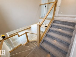 Carpeted staircase with recessed step lighting, glass panel railing with wood balusters, and light wood-finish flooring on the lower level - 