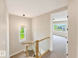 Staircase with light wood-finish handrails, glass balusters, and a contemporary chandelier - 