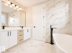 Contemporary bathroom featuring a freestanding tub with a matte black floor-mounted faucet, a dual vanity with white and wood-finish cabinetry, a large frameless mirror, and a linear light fixture with globe bulbs - 