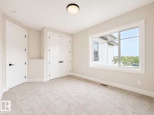 Carpeted room featuring a large window, white trim, and two white doors with black hardware - 16 Middleton Close, Leduc, AB 
