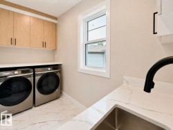 Laundry area featuring light wood-finish cabinetry, a white countertop, and a stainless steel sink with a matte black faucet - 