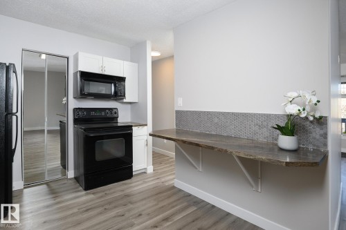 Kitchen featuring wood-finish flooring, a black range, a built-in microwave, white cabinetry, and a mirrored closet door - 5816 172 Street, Edmonton, AB - Indoor With Fireplace