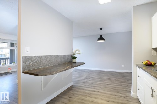 Breakfast bar with a stone-look countertop, hexagonal tile backsplash, and light wood-finish flooring - 5816 172 Street, Edmonton, AB - Indoor Photo Showing Other Room