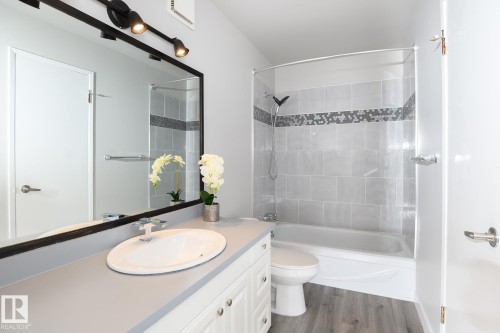 Bathroom featuring a vanity with an oval sink, track lighting, a full-width mirror, a shower-over-tub with glass enclosure, and wood-finish flooring - 5816 172 Street, Edmonton, AB - Indoor Photo Showing Bathroom