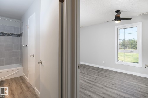 Spacious room featuring wood-finish flooring, a large window with grid pattern, and an overhead ceiling fan - 5816 172 Street, Edmonton, AB - Indoor