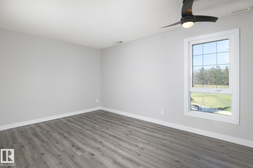 Spacious room with wood-finish flooring, a contemporary ceiling fan with integrated lighting, and a large window featuring white trim - 5816 172 Street, Edmonton, AB - Indoor Photo Showing Other Room