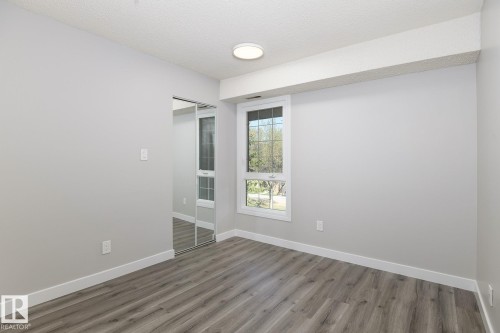 Bright room featuring wood-finish flooring, a contemporary ceiling light fixture, a window with exterior tree scenery, white trim, and a mirrored closet - 5816 172 Street, Edmonton, AB - Indoor Photo Showing Other Room