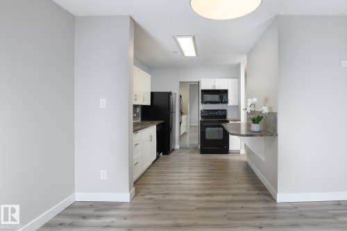 Kitchen with white cabinetry, black appliances, dark countertops, and a built-in breakfast bar with a tile backsplash - 5816 172 Street, Edmonton, AB - Indoor Photo Showing Kitchen
