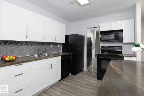 Kitchen featuring white cabinetry, dark wood-finish countertops, black appliances, and a hexagon tile backsplash - 5816 172 Street, Edmonton, AB - Indoor Photo Showing Kitchen With Double Sink