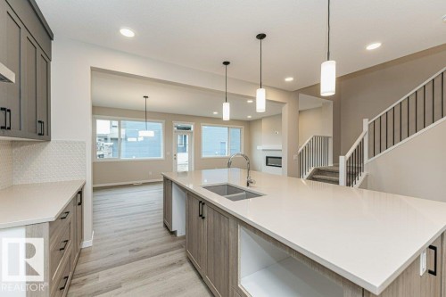 Modern kitchen featuring a large island with a double basin sink, light-colored countertops, and pendant lighting - 2616 158 Street, Edmonton, AB - Indoor Photo Showing Kitchen With Double Sink With Upgraded Kitchen