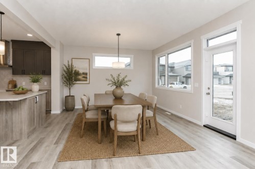 Dining area featuring wood-finish flooring, a contemporary pendant light fixture, and abundant natural light from multiple windows and a glass-paneled exterior door - 2616 158 Street, Edmonton, AB - Indoor Photo Showing Dining Room