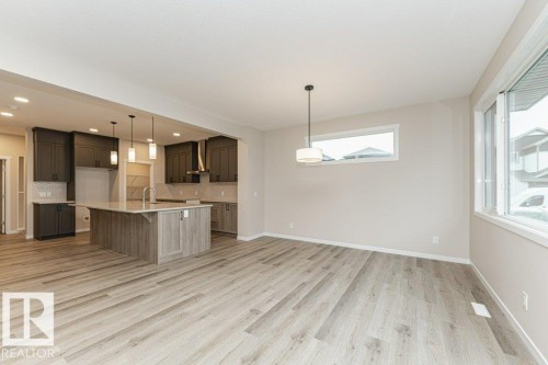 Open-concept living space featuring wood-finish flooring, a kitchen island with seating, dark wood cabinetry, a tile backsplash, and recessed lighting - 2616 158 Street, Edmonton, AB - Indoor Photo Showing Kitchen
