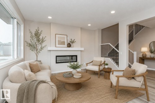 Spacious living area featuring a linear electric fireplace with a white mantel, large window, recessed lighting, wood-finish flooring, and a staircase with black metal balusters - 2616 158 Street, Edmonton, AB - Indoor Photo Showing Living Room With Fireplace