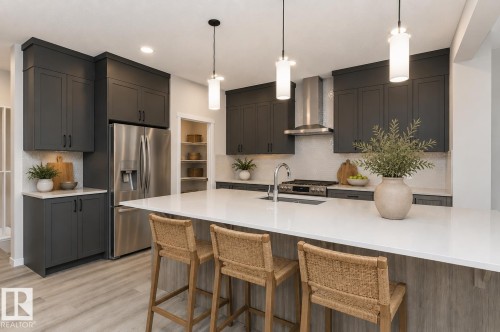 Contemporary kitchen featuring an expansive island with a white countertop and seating, dark cabinetry, stainless steel appliances, a tile backsplash, and light wood-finish flooring - 2616 158 Street, Edmonton, AB - Indoor Photo Showing Kitchen With Stainless Steel Kitchen With Upgraded Kitchen