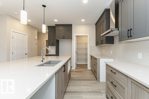 Contemporary kitchen featuring an expansive island with an integrated sink, white countertops, two-tone cabinetry, a mosaic tile backsplash, and light wood-finish flooring - 2616 158 Street, Edmonton, AB - Indoor Photo Showing Kitchen With Double Sink With Upgraded Kitchen