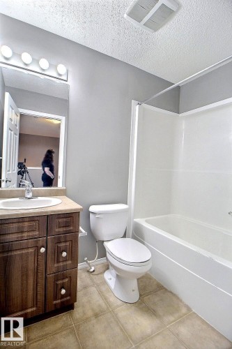 Bathroom featuring a wood-finish vanity with a light-colored countertop, a white toilet, and a white bathtub with a shower surround - 170 Keystone Crescent, Leduc, AB - Indoor Photo Showing Bathroom