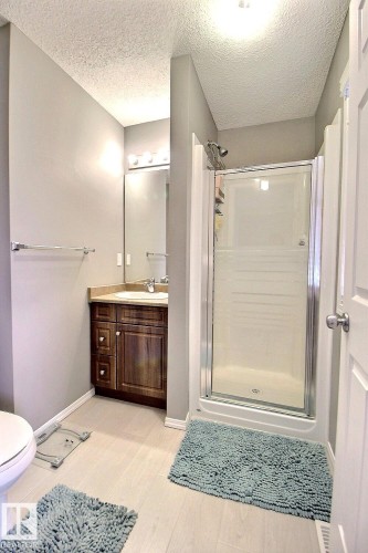 Bathroom featuring a glass-enclosed shower, a wood-finish vanity with an undermount sink, a large wall-mounted mirror, and wood-finish flooring - 170 Keystone Crescent, Leduc, AB - Indoor Photo Showing Bathroom