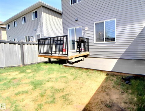 Rear exterior featuring a raised wooden deck with black metal railings, a ground-level patio, and gray horizontal siding - 170 Keystone Crescent, Leduc, AB - Outdoor With Exterior