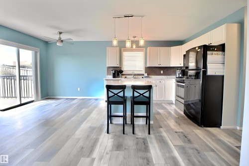Open-concept living space featuring wood-finish flooring, a contemporary ceiling fan, and sliding glass doors to a balcony - 170 Keystone Crescent, Leduc, AB - Indoor Photo Showing Kitchen With Double Sink