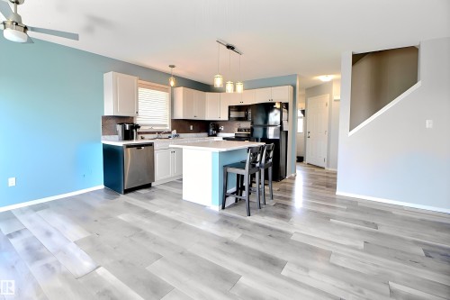 Open-concept kitchen featuring white cabinetry, an island with seating, a stainless steel dishwasher, black appliances, and pendant lighting - 170 Keystone Crescent, Leduc, AB - Indoor Photo Showing Kitchen