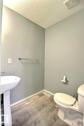 Powder room featuring a pedestal sink, white toilet, wood-finish flooring, and light gray walls - 170 Keystone Crescent, Leduc, AB - Indoor Photo Showing Bathroom