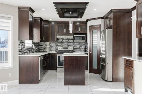Kitchen featuring dark wood cabinetry, stainless steel appliances, a mosaic tile backsplash, and a central island with a contrasting countertop - 4831 154 Avenue, Edmonton, AB - Indoor Photo Showing Kitchen With Upgraded Kitchen