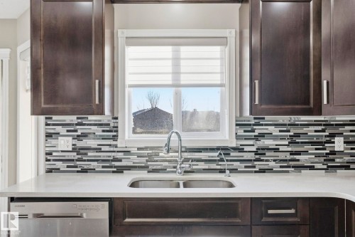 Kitchen featuring dark wood cabinetry, a dual basin stainless steel sink with a chrome faucet, and a decorative backsplash - 4831 154 Avenue, Edmonton, AB - Indoor Photo Showing Kitchen With Double Sink With Upgraded Kitchen