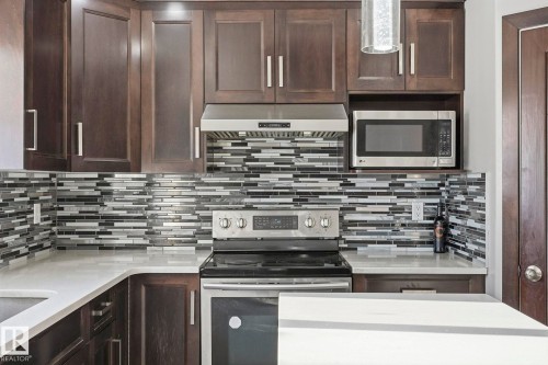 The kitchen features rich dark cabinetry, a striking mosaic tile backsplash, and stainless steel appliances, including a built-in microwave and range - 4831 154 Avenue, Edmonton, AB - Indoor Photo Showing Kitchen