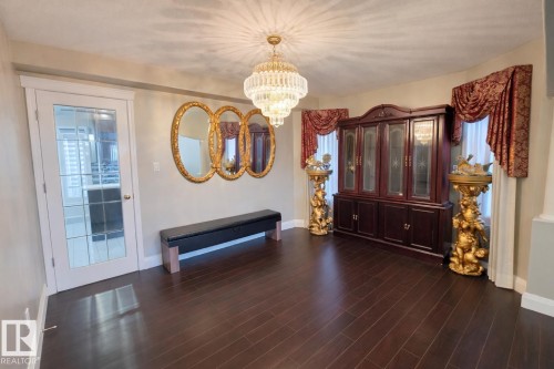 This space features dark hardwood flooring, a prominent crystal chandelier, and a white framed glass door - 4831 154 Avenue, Edmonton, AB - Indoor