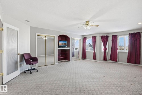 Spacious room featuring light gray carpet flooring, multiple windows providing natural light, and a built-in media cabinet with shelving - 4831 154 Avenue, Edmonton, AB - Indoor Photo Showing Bedroom