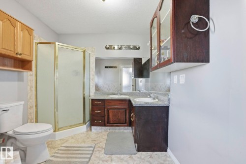 This bathroom features a shower enclosure with gold-toned framing, a toilet, and dual vanity sinks with granite-style countertops - 4831 154 Avenue, Edmonton, AB - Indoor Photo Showing Bathroom