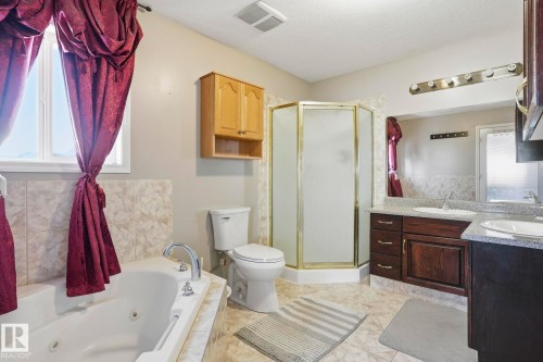 The bathroom features a corner shower with a glass enclosure, a white toilet, and a vanity with a dark wood finish and double sinks - 4831 154 Avenue, Edmonton, AB - Indoor Photo Showing Bathroom