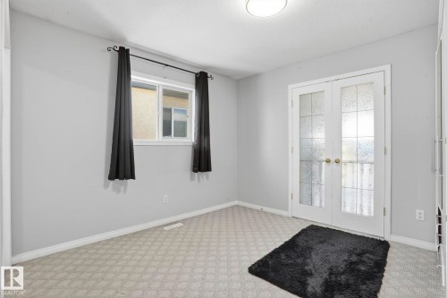 Room featuring light gray walls, patterned carpet, a window with black curtains, and white French doors with frosted glass panels - 4831 154 Avenue, Edmonton, AB - Indoor Photo Showing Other Room