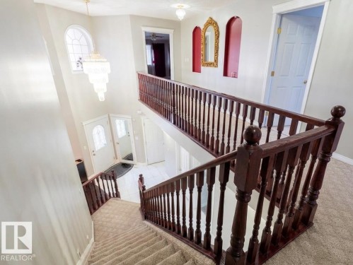 The property features a grand two-story entry with a decorative chandelier, arched window, and a carpeted staircase with a dark wood railing - 4831 154 Avenue, Edmonton, AB - Indoor Photo Showing Other Room