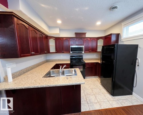 The kitchen features dark wood cabinetry, light-colored countertops, and stainless steel appliances including a microwave, range, and refrigerator - 4831 154 Avenue, Edmonton, AB - Indoor Photo Showing Kitchen With Double Sink