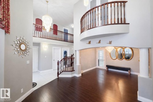 This grand foyer features high ceilings, dark hardwood flooring, and a curved balcony with a wooden railing overlooking the space - 4831 154 Avenue, Edmonton, AB - Indoor Photo Showing Other Room