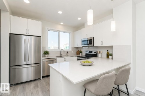Kitchen featuring white cabinetry, stainless steel appliances, a white countertop island with seating, a stainless steel sink, and wood-finish flooring - 3896 Wren Crescent, Edmonton, AB - Indoor Photo Showing Kitchen With Stainless Steel Kitchen With Double Sink With Upgraded Kitchen