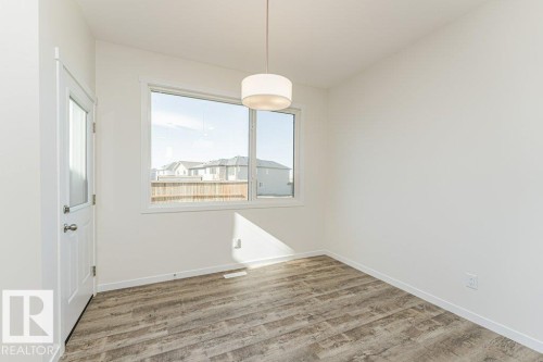 Bright interior space featuring a drum pendant light fixture, wood-finish flooring, white baseboards, and a window with white trim - 6271 180 Avenue, Edmonton, AB - Indoor Photo Showing Other Room