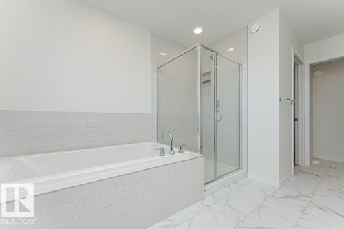 Contemporary bathroom featuring a built-in tub with deck-mounted fixtures, a glass-enclosed shower, white subway tile wainscoting, white walls, and white-patterned floor tiling - 6271 180 Avenue, Edmonton, AB - Indoor Photo Showing Bathroom