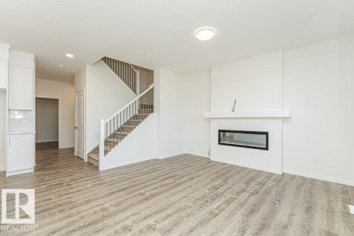 Living area featuring wood-finish flooring, a contemporary fireplace with a white mantel, and a staircase with carpeted treads and white railings - 6271 180 Avenue, Edmonton, AB - Indoor With Fireplace
