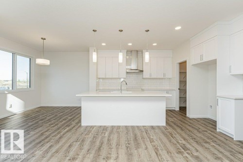 Bright kitchen featuring white cabinetry, a central island with a sink, stainless steel appliances including a range hood, and a white subway tile backsplash - 6271 180 Avenue, Edmonton, AB - Indoor Photo Showing Kitchen With Upgraded Kitchen