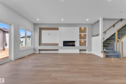 Spacious living area featuring light wood-finish flooring, a contemporary built-in media wall with an electric fireplace, recessed lighting, and large windows - 3116 8 Avenue, Edmonton, AB - Indoor Photo Showing Other Room