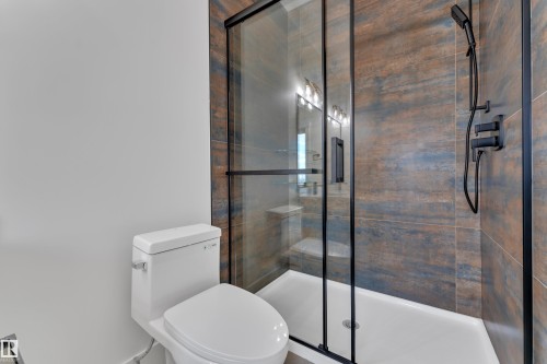 Bathroom featuring a glass-enclosed shower with matte black fixtures, a white shower pan, and large format wall tiling in earthy tones - 3116 8 Avenue, Edmonton, AB - Indoor Photo Showing Bathroom