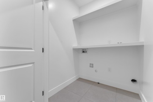 Dedicated laundry room featuring light gray floor tiles, crisp white walls, built-in shelving, and utility hookups - 3116 8 Avenue, Edmonton, AB - Indoor