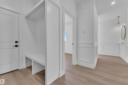 Entryway featuring built-in bench storage, wood-finish flooring, white paneled walls, and a modern pendant light fixture - 3116 8 Avenue, Edmonton, AB - Indoor Photo Showing Other Room
