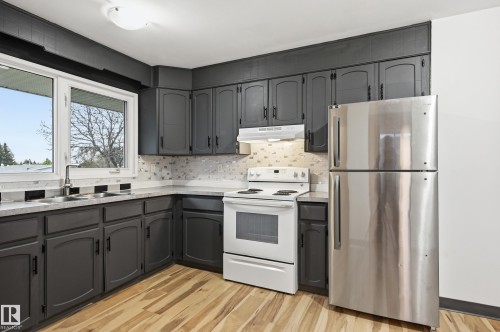 Kitchen featuring dark cabinetry with black hardware, light-toned countertops, and a mosaic tile backsplash - 13903 87 Street, Edmonton, AB - Indoor Photo Showing Kitchen With Double Sink