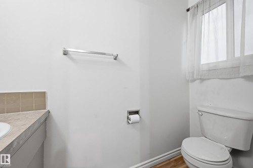 Bathroom featuring a window with sheer curtains, a white toilet, and a vanity with a light-colored countertop and tiled backsplash - 13903 87 Street, Edmonton, AB - Indoor Photo Showing Bathroom