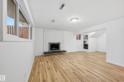 Spacious room featuring wood-finish flooring, a white brick fireplace with a dark hearth, built-in shelving, and white walls - 