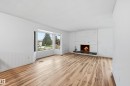 Spacious interior featuring wide-plank wood-finish flooring, a white painted brick fireplace with a dark stone hearth, and a multi-pane bay window - 13903 87 Street, Edmonton, AB  - Indoor Photo Showing Living Room With Fireplace 